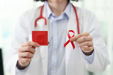 Doctor holds condom in wrapper and red ribbon in hands