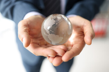 Man in business suit holds glass globe with continents