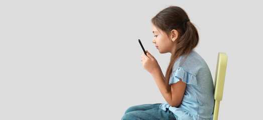 Little girl with bad posture using mobile phone on light background - obrazy, fototapety, plakaty