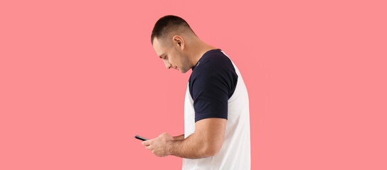 Young man with bad posture using mobile phone on pink background
