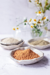 Rhassoul cosmetic clay powder in ceramic plate on white marble background.