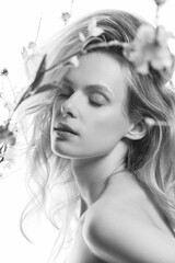 Beautiful blonde woman with big wavy hair and purple make-up studio portrait. Model surrounded with flower twigs with blossoms. Bright and glowing filter applied. Black and white image