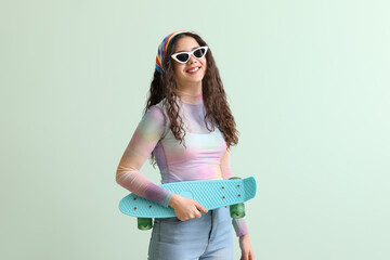 Teenage girl in sunglasses with skateboard on green background