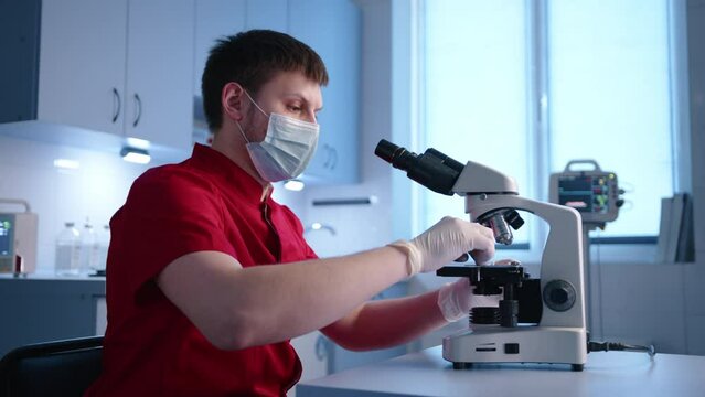 Male young competent vet is focused on laboratory research using binocular microscope. The doctor sets up microscope and conducts research. High quality 4k footage