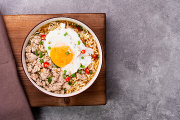 Instant noodles or ramen with minced pork and boiled egg in white bowl on the table with copy space - top view