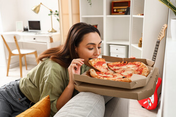 Beautiful woman eating tasty pizza on sofa at home