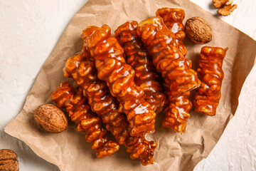 Paper sheet with tasty churchkhela and walnuts on light background, closeup