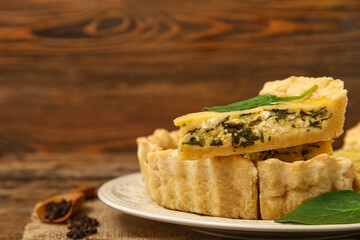 Plate with pieces of delicious quiche on brown wooden background