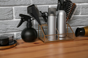 Different hair sprays and accessories on table near grey brick wall