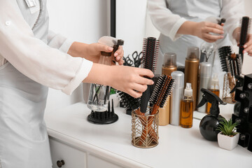 Woman with hair spray and brush at table in beauty salon, closeup