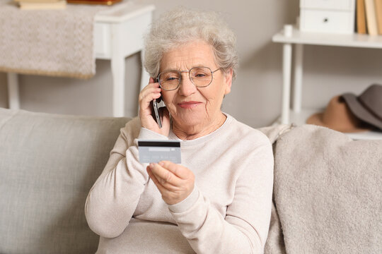 Senior woman with credit card talking by mobile phone on sofa at home