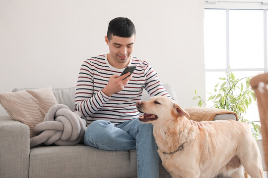 Young man with mobile phone taking picture of his Labrador dog at home