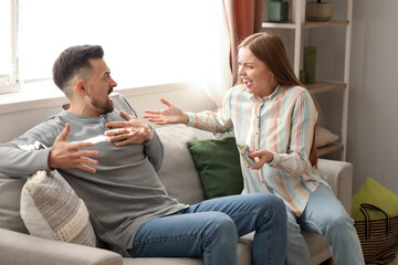 Angry young woman with money shouting at her husband at home. Domestic violence concept