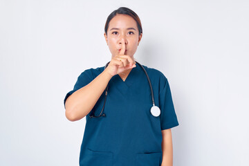 Serious young Asian female nurse working wearing a blue uniform shows silence gestures isolated on white background. Healthcare medicine concept