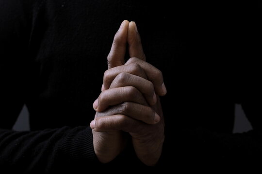 man praying to god with hands together on dark background stock photo