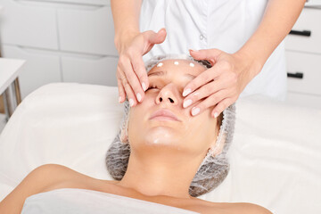 Cosmetologist rubbing moisturizing cream mask into woman face skin for rejuvenation, anti aging...