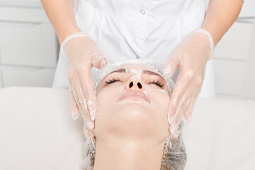 Beautician massages cream mask into female face skin for rejuvenation, moisturizing skincare...