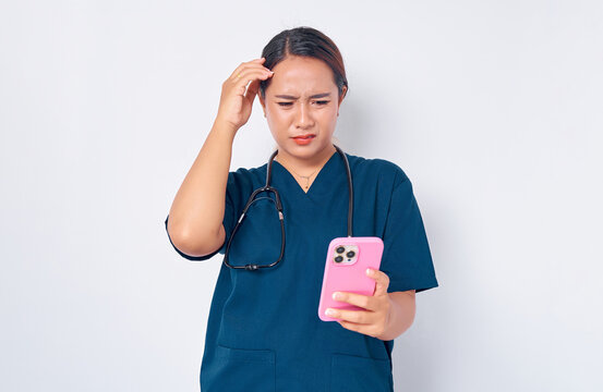 Confused young Asian woman nurse working wearing a blue uniform looking at smartphone screen and emotionally reacting to online news isolated on white background. Healthcare medicine concept