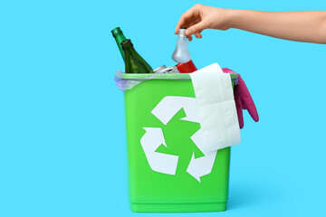 Woman throwing garbage into trash bin on blue background