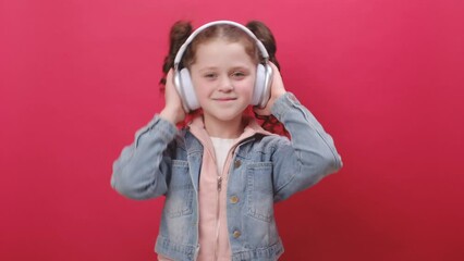 Portrait of cheerful preteen girl kid listening music via headphones and dancing disco fooling around having fun expressive gesticulating hands, posing isolated on red color background wall in studio