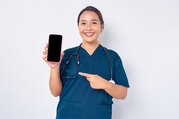 Smiling young Asian woman professional nurse working wearing a blue uniform pointing index finger at mobile phone with blank screen isolated on white background. Healthcare medicine concept