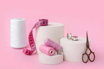 Podiums with tailor's supplies on pink background