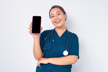 Smiling young Asian woman nurse working wearing a blue uniform showing smartphone with blank screen isolated on white background. Healthcare medicine concept