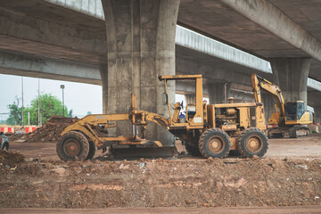 Obraz premium Grader tractor parked in highway construction area near concrete high bridge