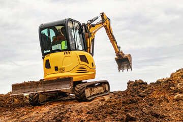 Mini excavator at the construction site on the edge of a pit against a cloudy blue sky. Compact construction equipment for earthworks. An indispensable assistant for earthworks.