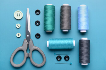 Composition with thread spools, buttons, scissors and ball pins on color background