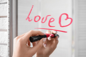 Female hand writing word LOVE with red lipstick on mirror