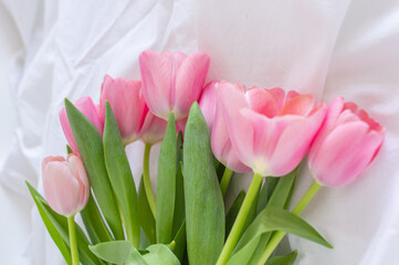 Pink tulips bouquet lying on white wrinkled blanket background copy space