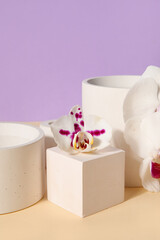 Decorative plaster podiums and beautiful orchid flower on beige table against lilac background