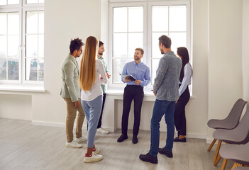Fototapeta premium Group of businesspeople talking to each other at office meeting. Cheerful colleagues brainstorming, analyzing financial results, developing strategy while standing in conference room