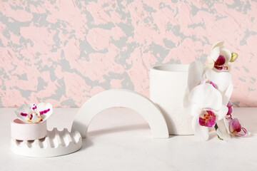 Decorative plaster podiums and beautiful orchid flowers on white table near pink wall