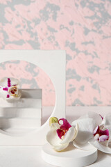 Decorative plaster podiums and beautiful orchid flowers on white table near pink wall