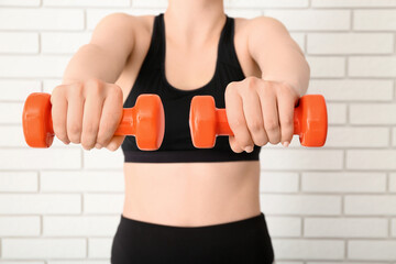 Sporty woman with dumbbells near white brick wall, closeup