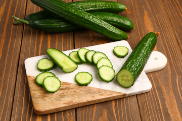 Board with fresh cut cucumber on wooden background