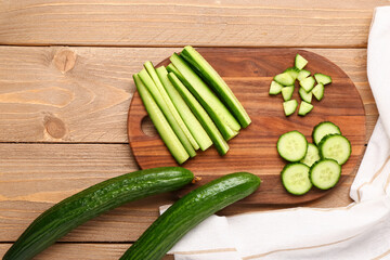 Board with cut and whole cucumbers on wooden background