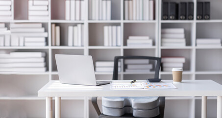 Laptop Computer, notebook, and eyeglasses sitting on a desk in a large open plan office space after working hours	