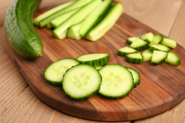 Board with fresh cut cucumber on wooden background, closeup