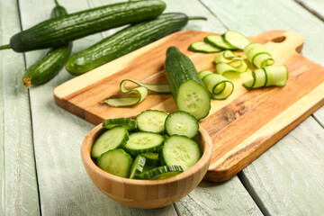 Bowl with fresh cut cucumber on light wooden background
