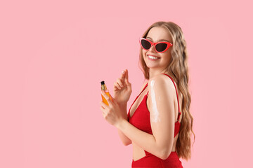 Beautiful young woman applying sunscreen cream on pink background