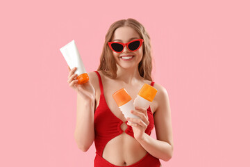 Beautiful young woman with sunscreen creams on pink background