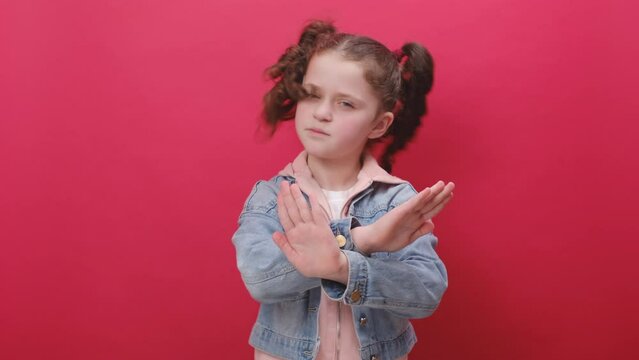 Portrait of serious little girl kid showing stop gesture, confused shy scared to watch, posing isolated over pastel red color background wall in studio. Dont want to look at this, awful concept