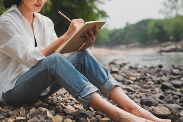 Close up of Female's hand is writing or sketching and idea while sitting and chilling by river....