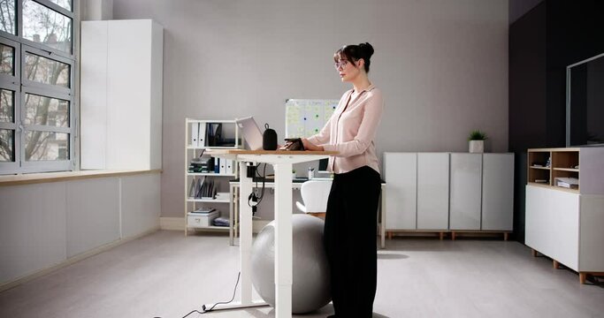 Woman Using Adjustable Height Standing Desk In Office