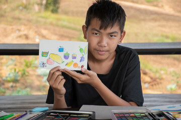 A boy in casual black clothes is showing his drawing and painting which he used small watercolor...
