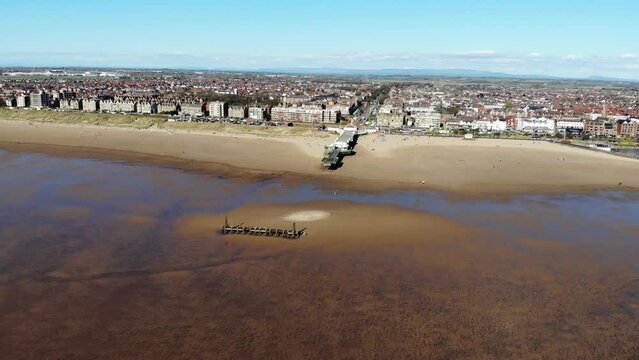 Aerial view rotation around the Lytham St Anne's piers at low tide with Blackpool tower in the distance