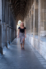 Fototapeta na wymiar Beautiful young blonde woman wearing stylish business attire and high heels walking inside a covered passage in a European city. High quality photo